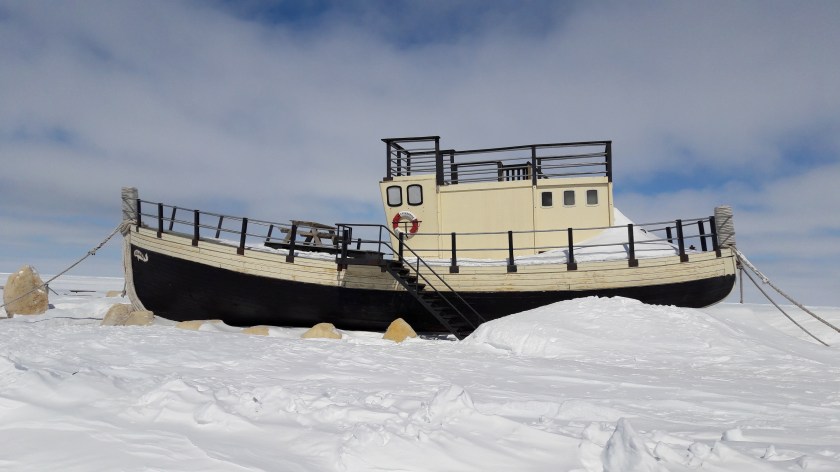 A little black and gold fishing boat, with steps leading up to it and a bench on top, moored and banked in by snow. You can't tell from the picture, but it was built in Buckie!