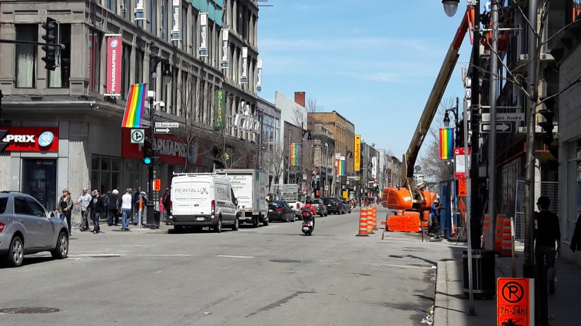 Le Village Gai, Montréal. There are igh street shops and a lot of condo construction; along the street, rainbow flags are visible. In the distance, things get pleasantly seedier.